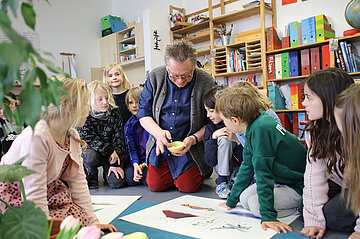 Montessori Lehrer sitz neben Schülerinnen und Schülern