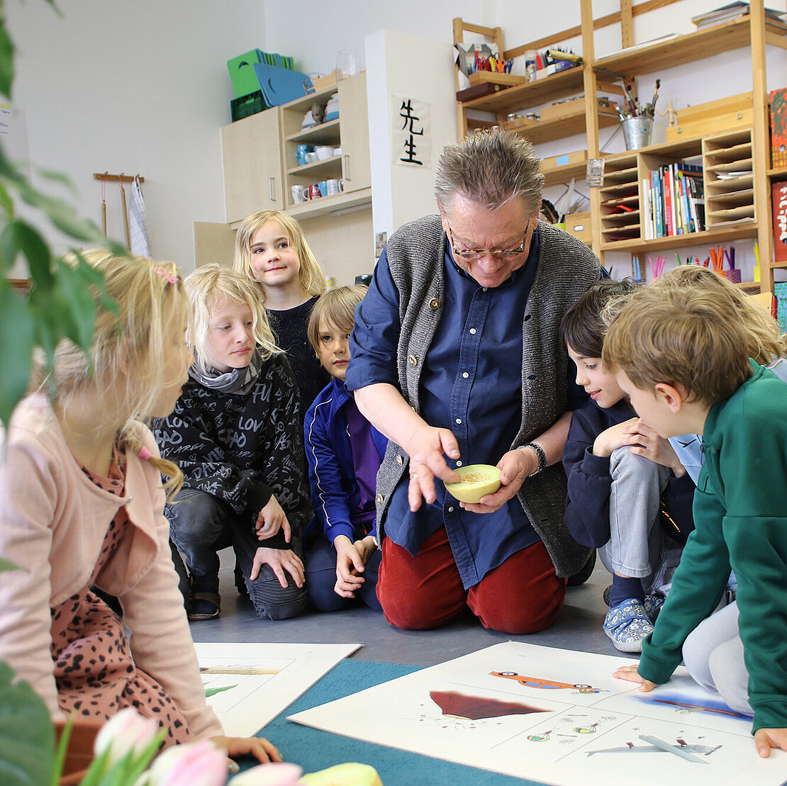 Montessori Lehrer sitz neben Schülerinnen und Schülern