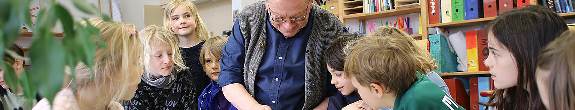Montessori Lehrer sitz neben Schülerinnen und Schülern