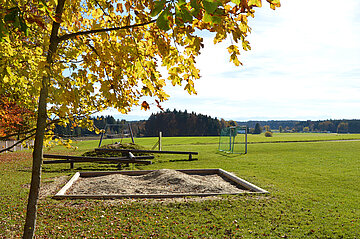Sandkasten eingelassen in einer Wiese auf dem Spielplatz der Montessori Schule
